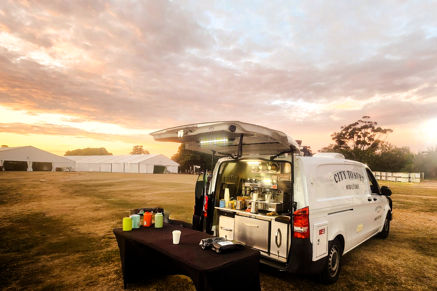 The Merc — a white Mercedes long-wheelbase coffee van at a festival site at sunset